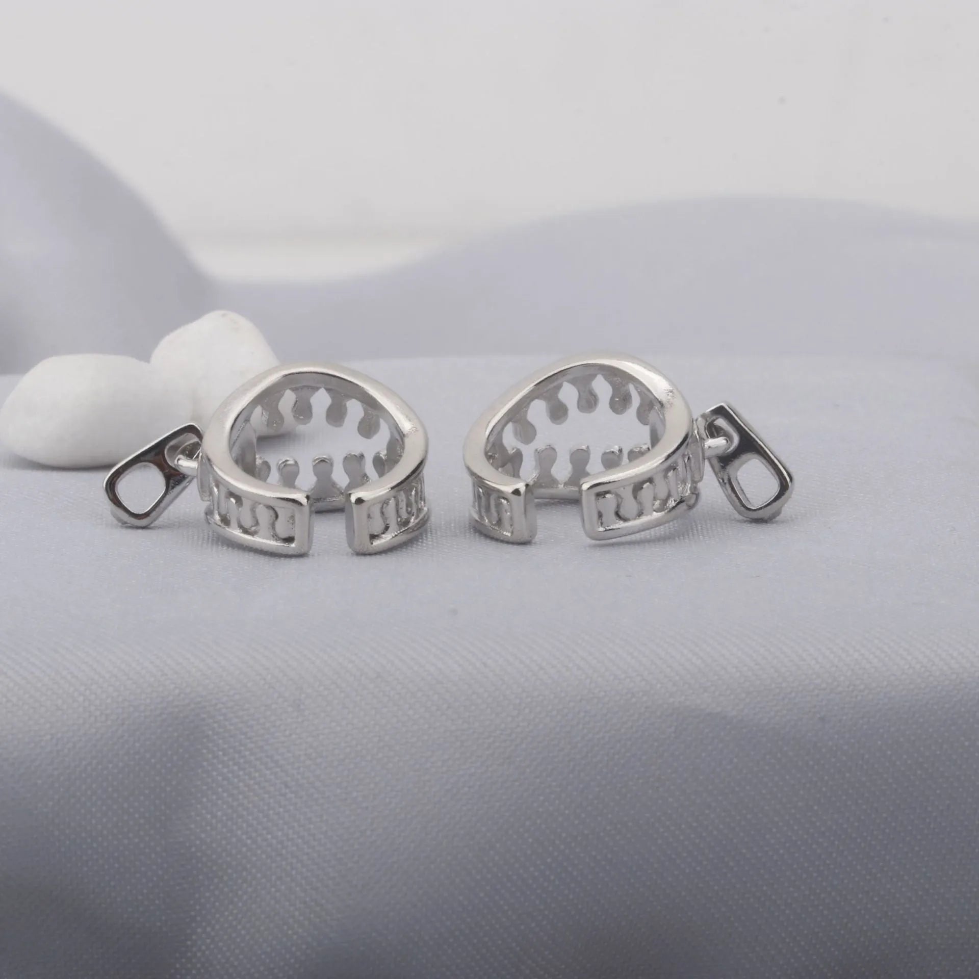 A pair of silver-tone geometric openwork clip-on earrings with a zipper design detail.