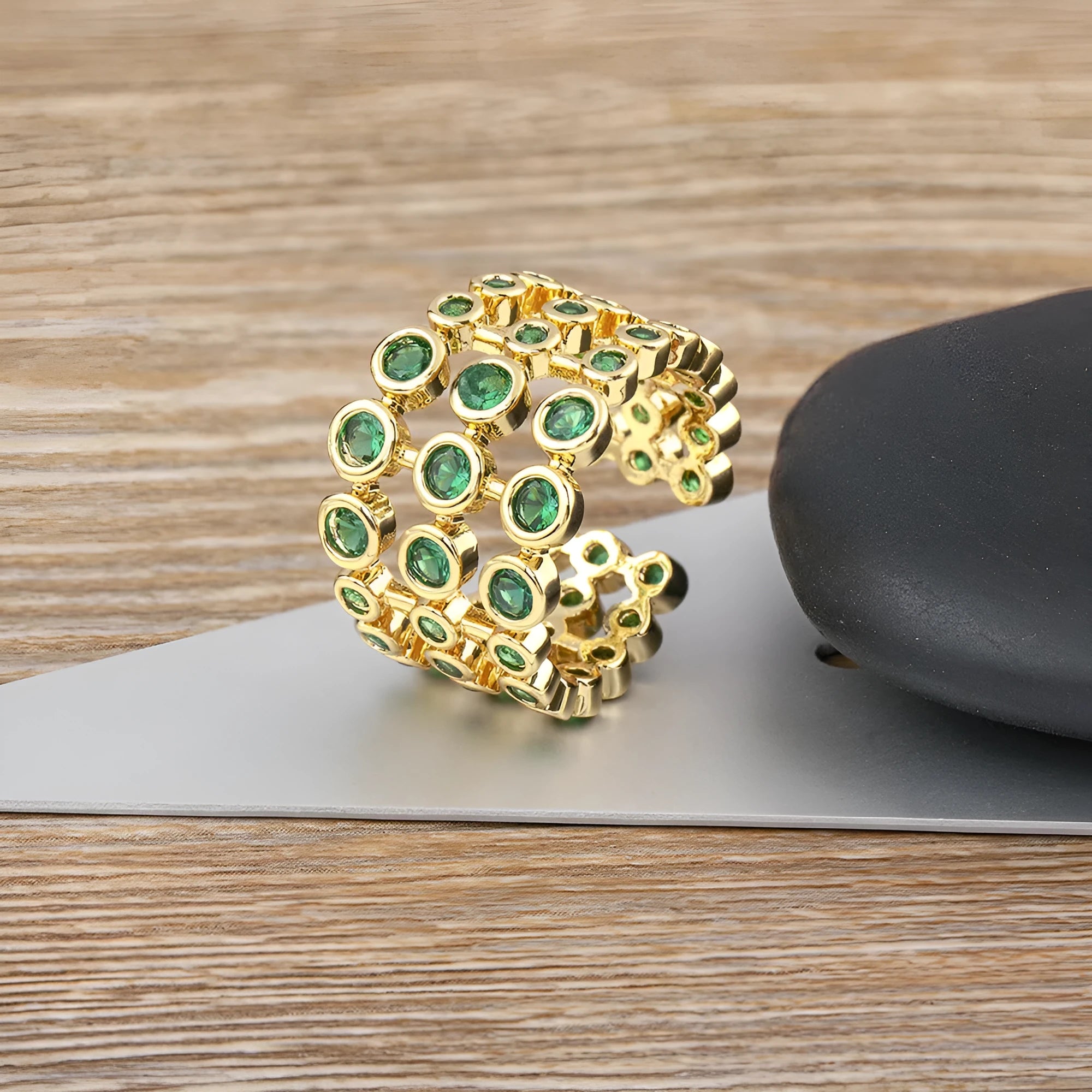 Copper and gold plated wide band ring with green zircon stones on a white background.