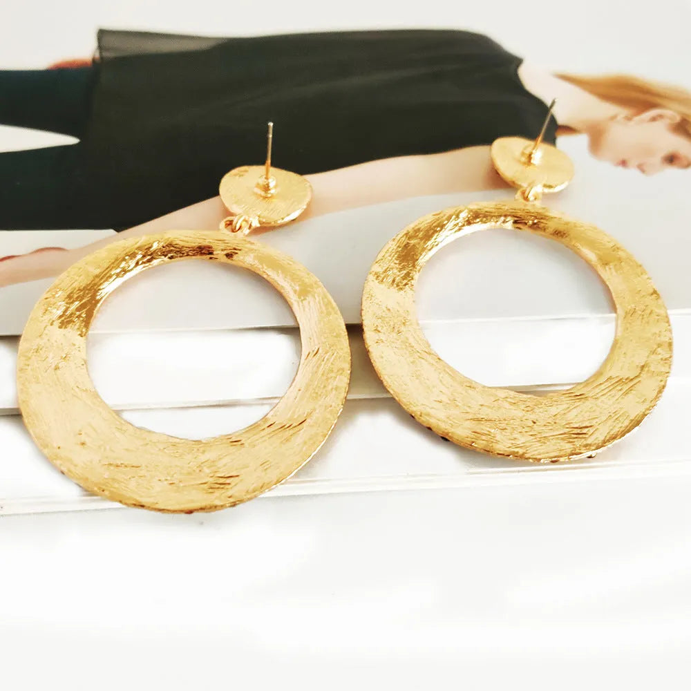 A pair of large round metal pendant earrings with diamond detailing in a cartoon style.