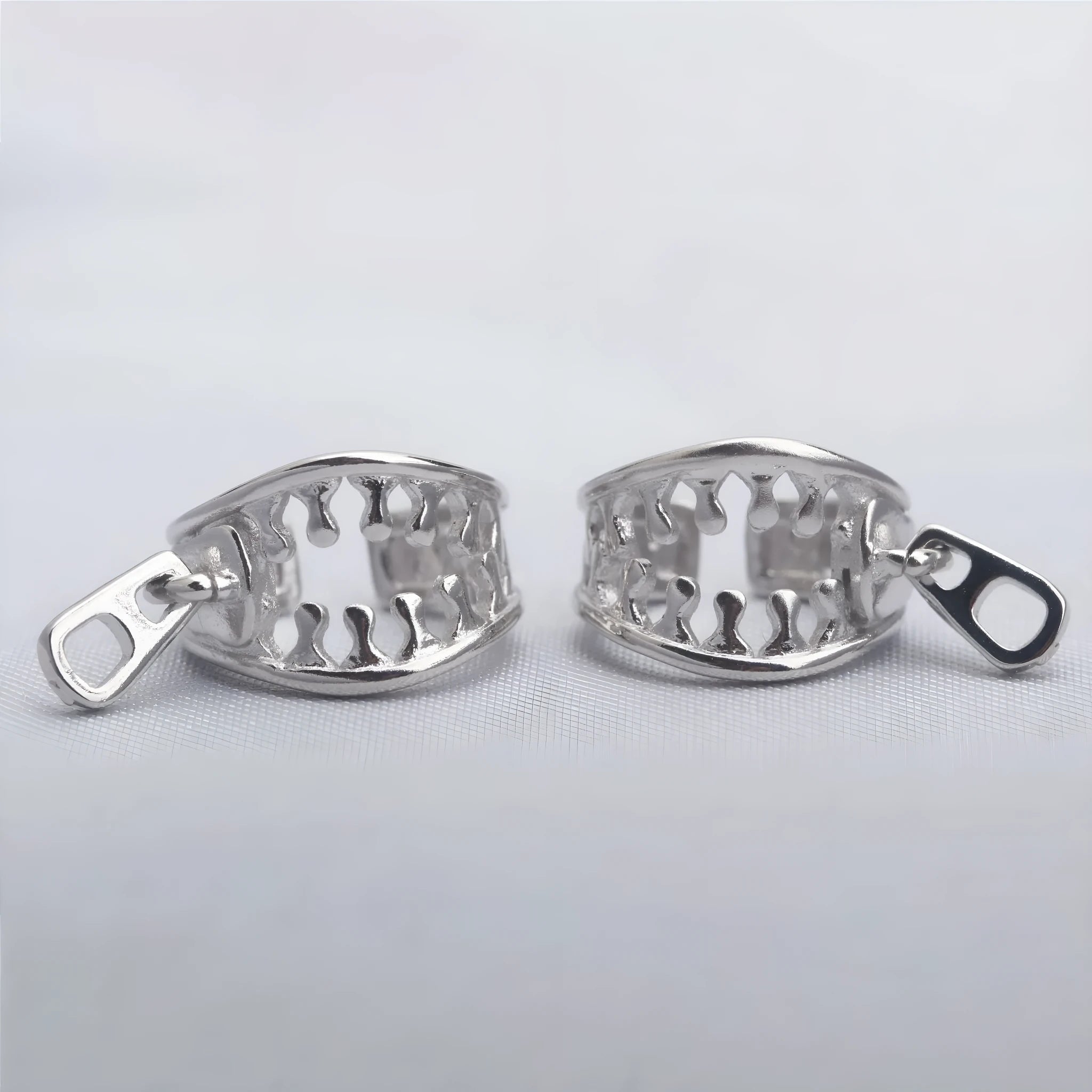 A pair of silver-tone geometric openwork clip-on earrings with a zipper design detail.