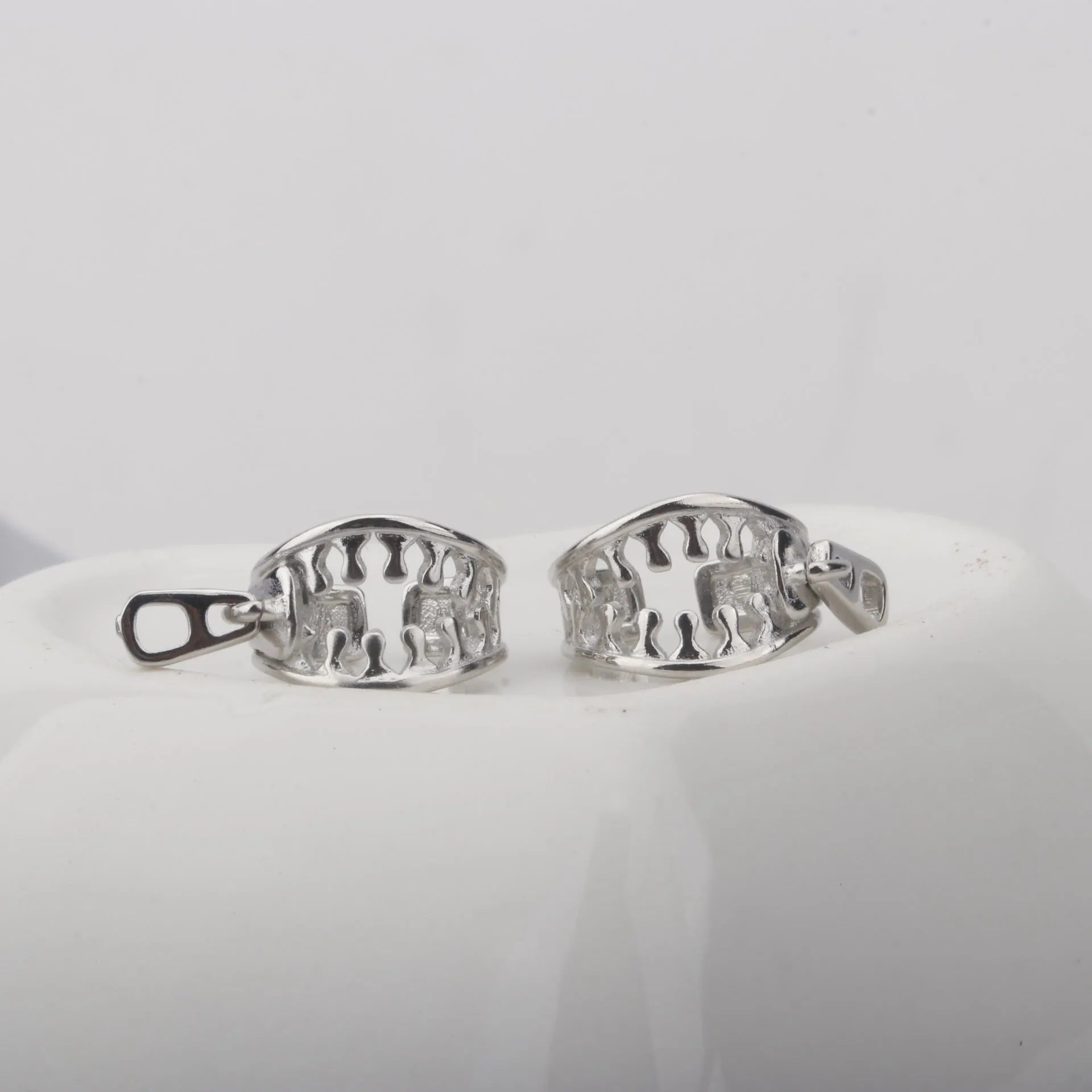 A pair of silver-tone geometric openwork clip-on earrings with a zipper design detail.