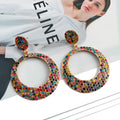 A pair of large round metal pendant earrings with diamond detailing in a cartoon style.
