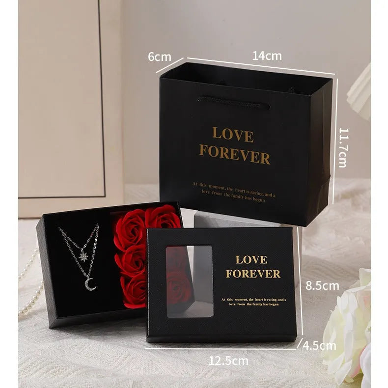 Red, pink, and black soap flower gift sets presented in a box with a handbag-style carrier.