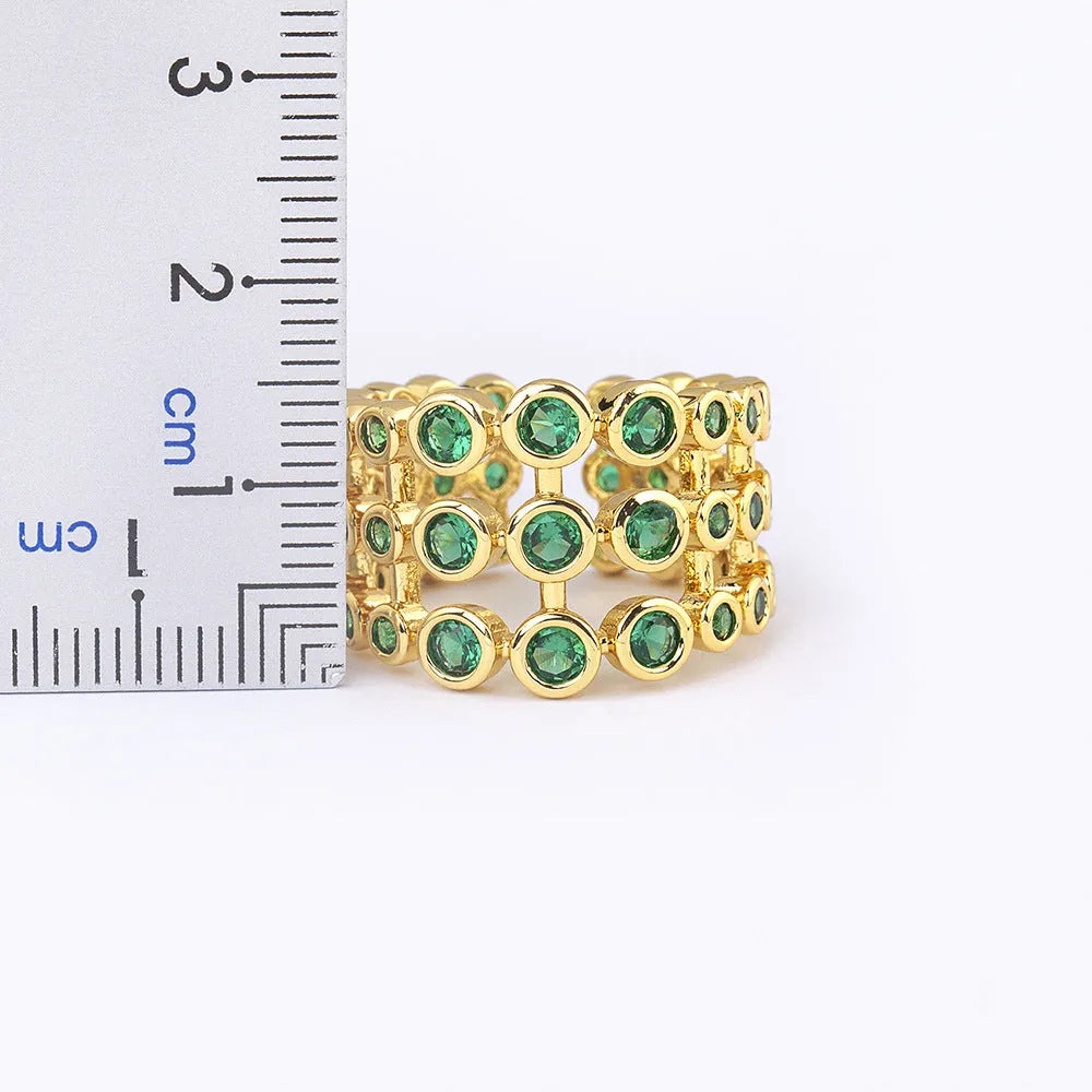 Copper and gold plated wide band ring with green zircon stones on a white background.
