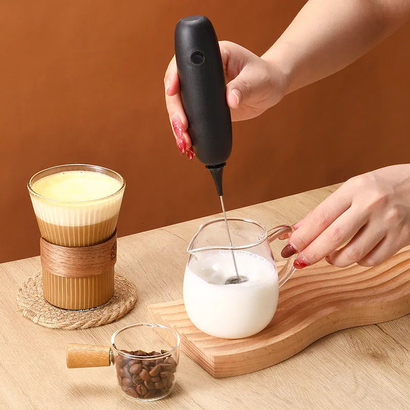 Black and white handheld electric milk frother with whisk attachment for coffee drinks