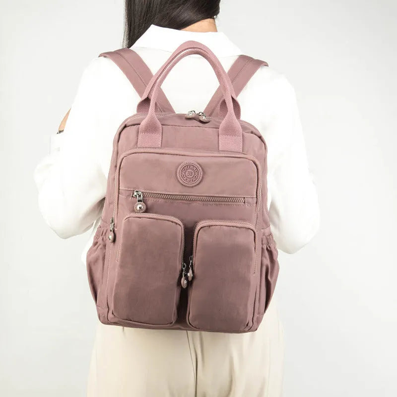 Waterproof women's travel backpack in grey showing front three-dimensional pocket and internal organiser compartments.