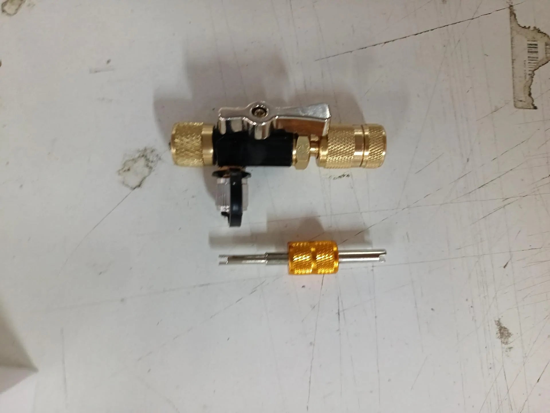 Metal vacuum valve core disassembly tool set showing black and pink valve removers and a valve core wrench on a workshop bench.