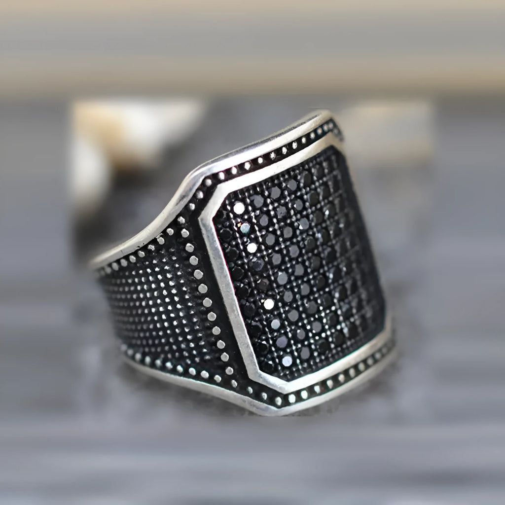Black alloy ring with copper inlay detail and set zircon stones, shown on a hand.