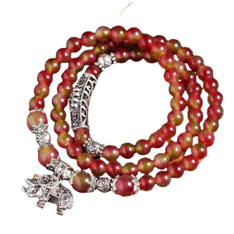 Handmade bracelet with watermelon crystal beads and a red Chinese knot on a white background.