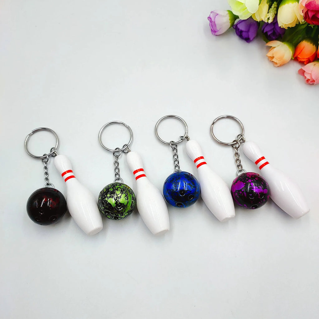 Miniature blue bowling ball keychain pendant with metal keyring on a dark surface.