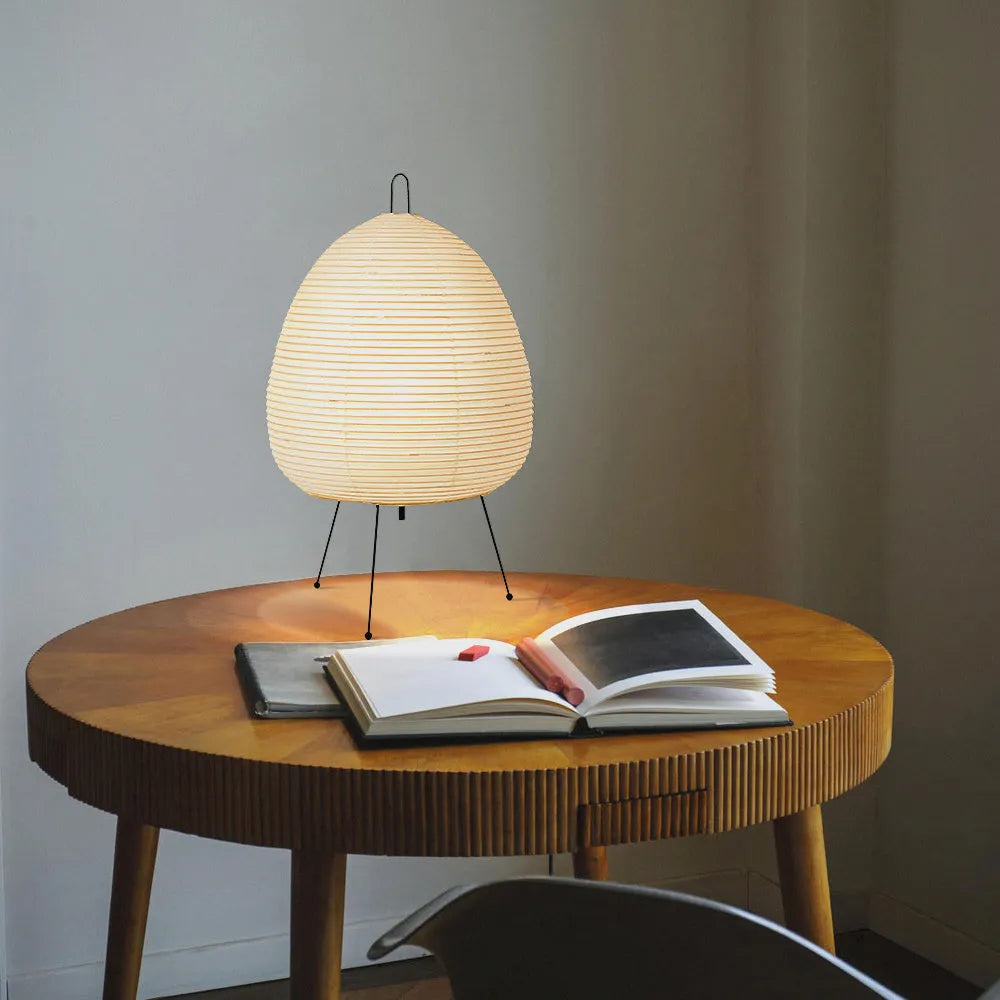 Japanese style table lamp with a white handmade paper lantern shade and aluminium base on a wooden table.