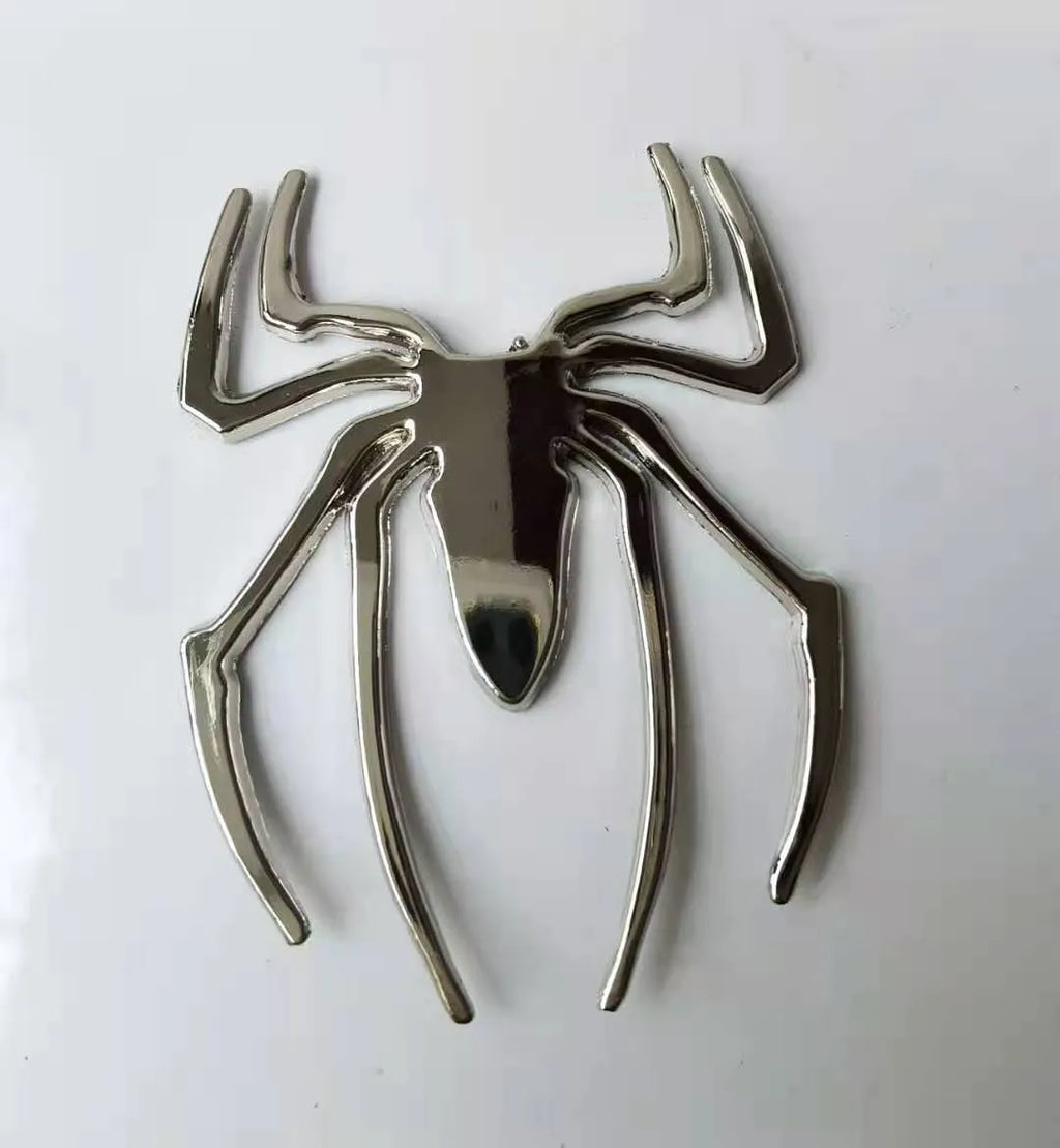 Three-dimensional zinc alloy spider bumper sticker in metallic colours on a surface.