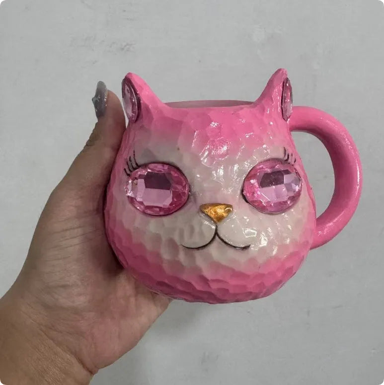 Small resin cat cup figurine in purple, green, blue, or pink colour on a shelf.