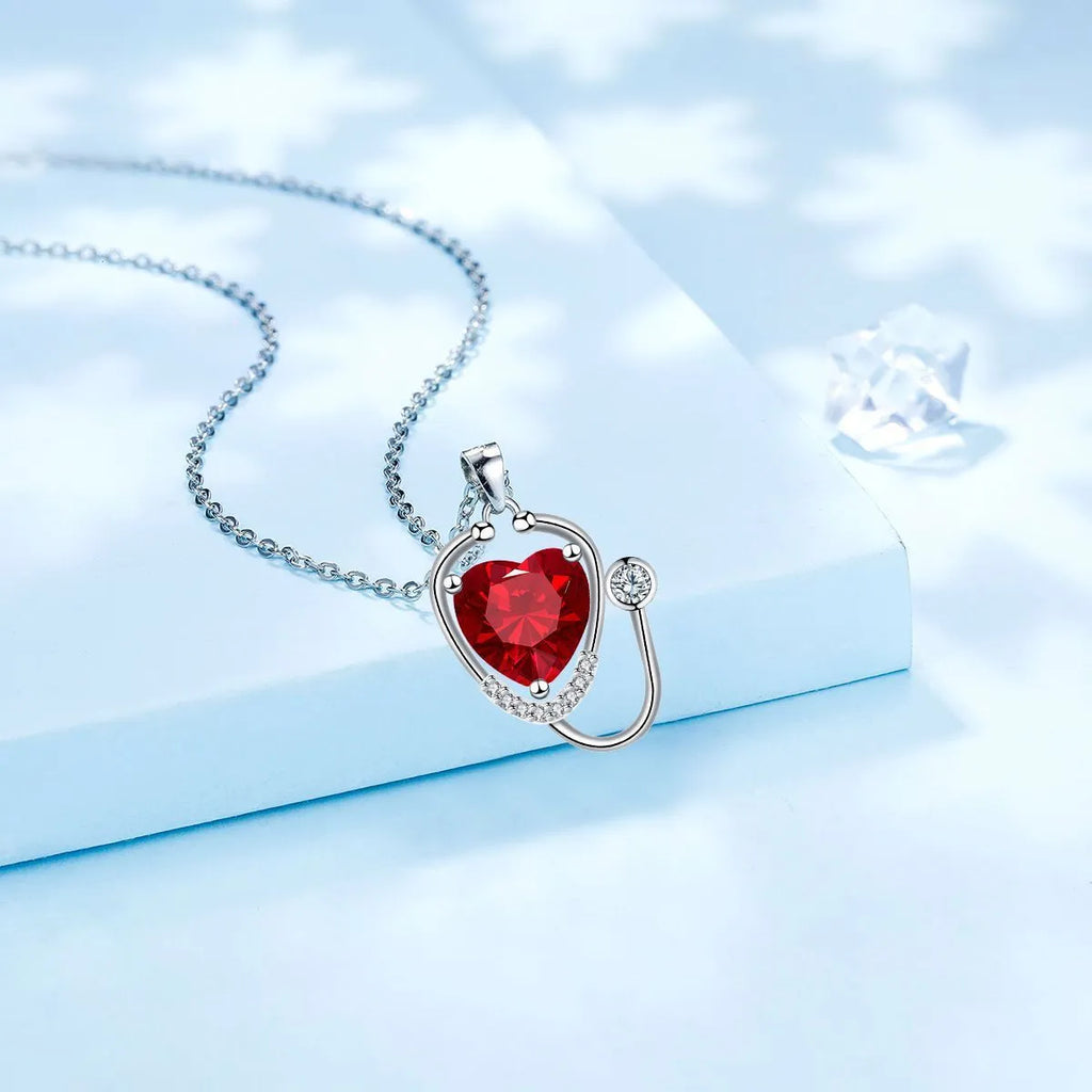 Close-up of a red diamond coloured stethoscope pendant necklace with cross, heart and wing details on a copper chain.