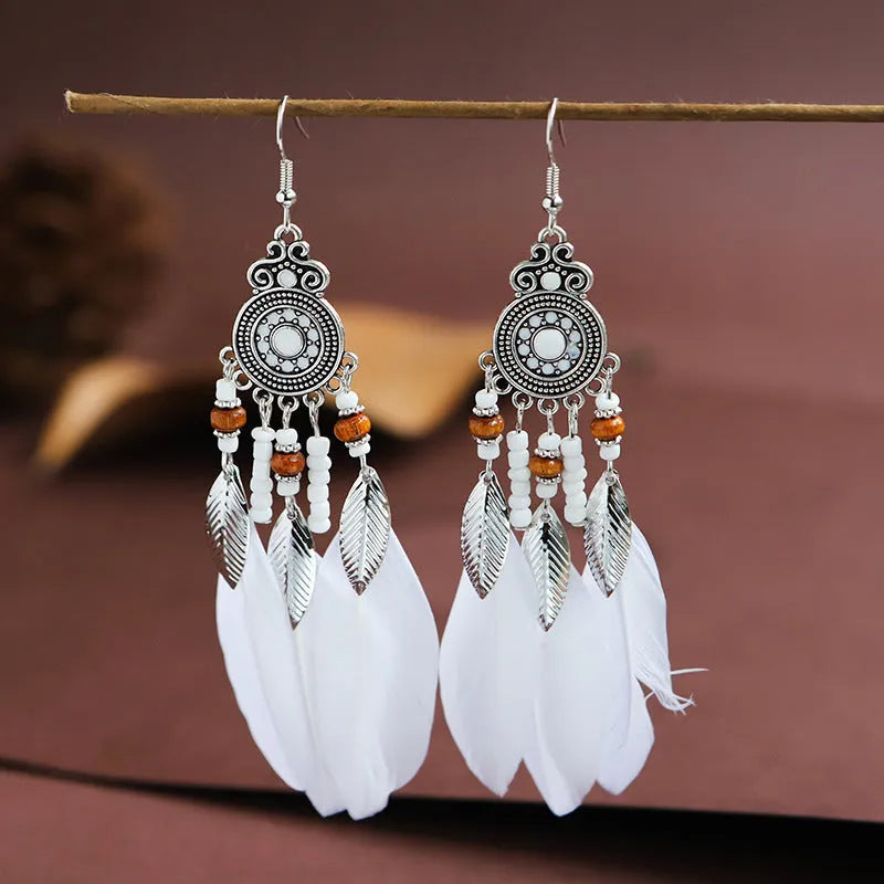 Close-up of a pair of bohemian-style feather-shaped earrings with a leaf pattern, in an alloy electroplated finish.