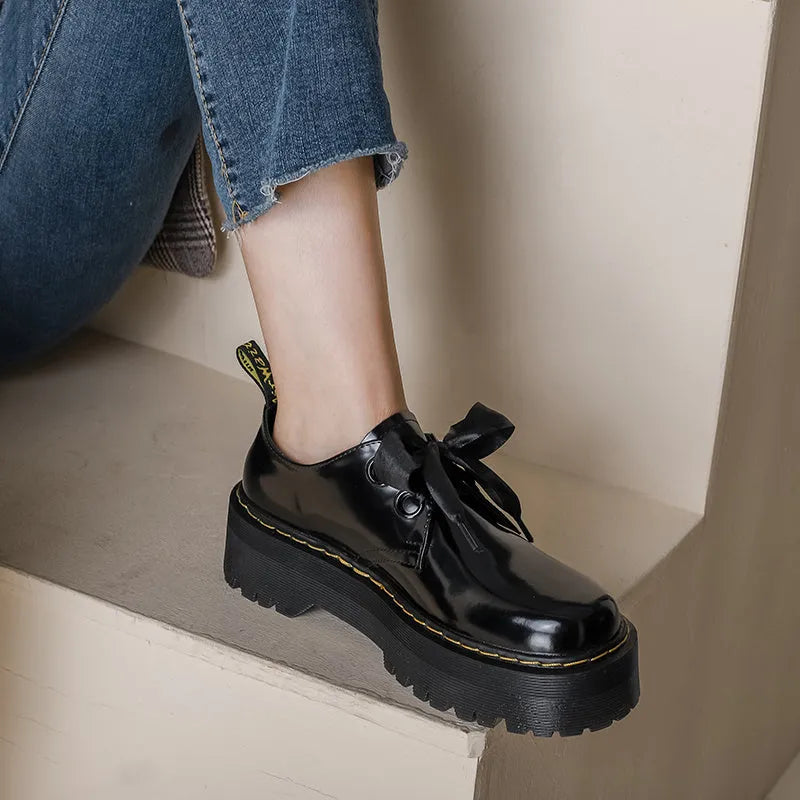 Women's black leather shoes with thick soles, cross straps featuring ribbon details, and lace-up closure