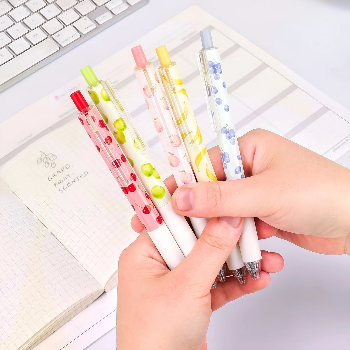 Three fruit-themed scented pressurised pens with 0.5mm black ink refills on writing surface