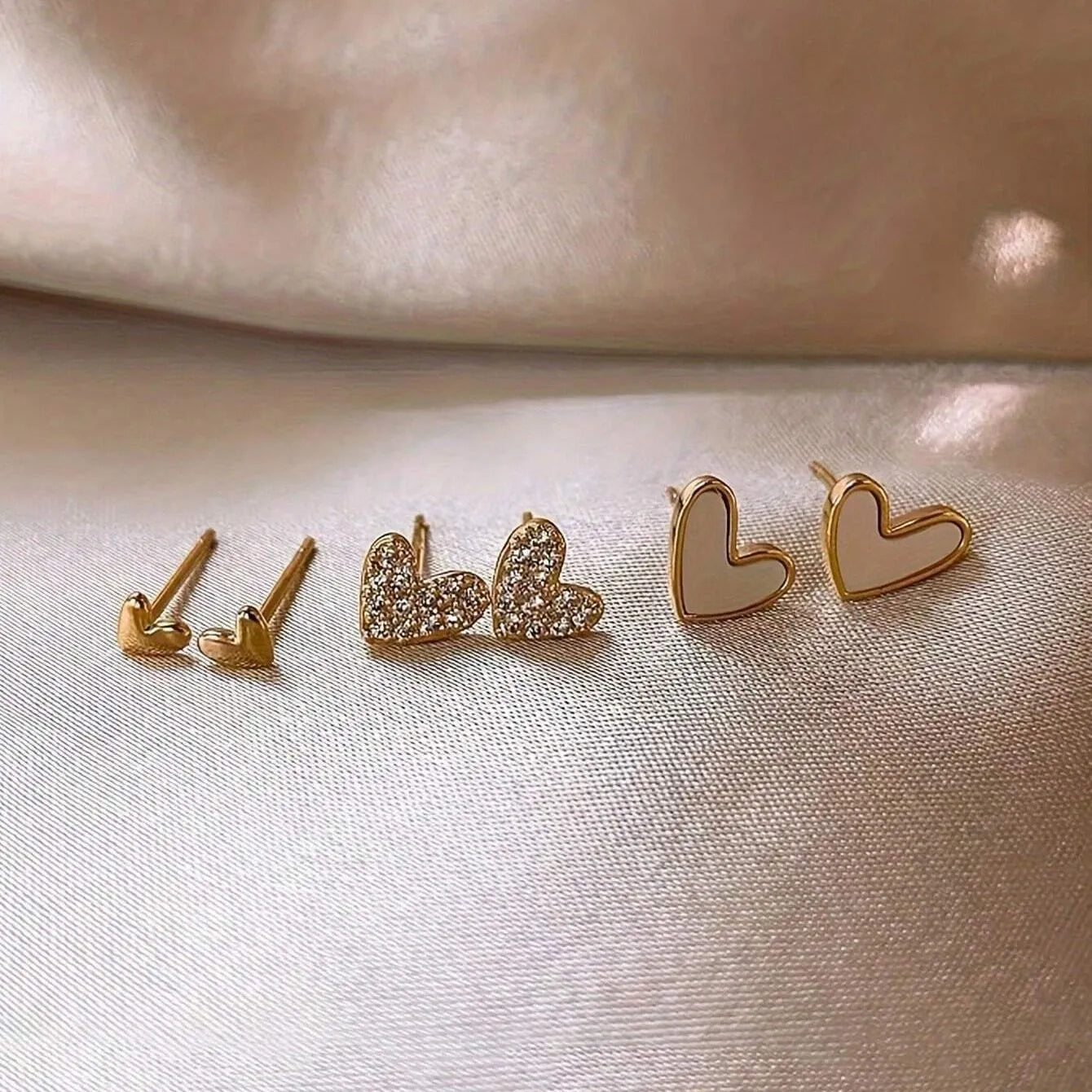 Three pairs of women's heart-shaped alloy earrings in gold, black, white and pink electroplated finishes
