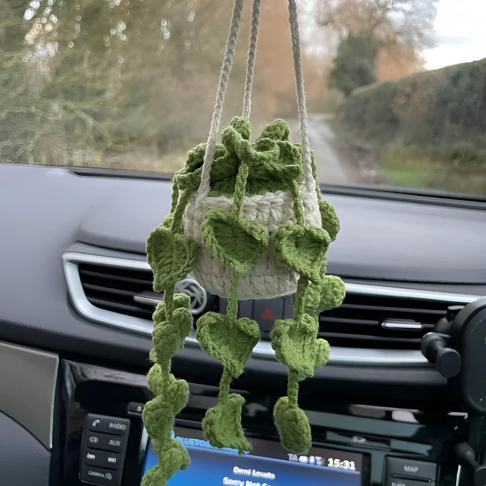 Green and white knitted car plant decoration with hanging rope on car dashboard