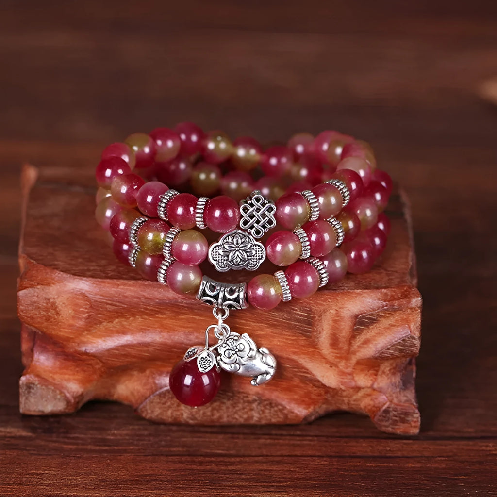 Handmade bracelet with watermelon crystal beads and a red Chinese knot on a white background.