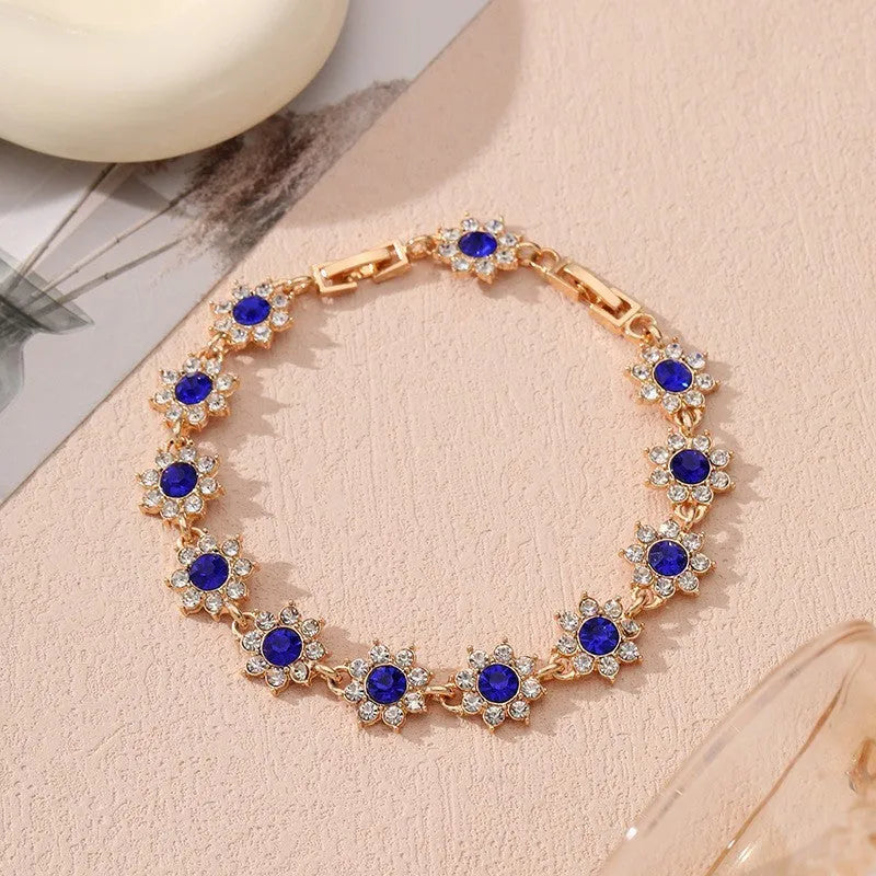 Gold tone flower-shaped bracelet with blue crystal gems on a wrist.