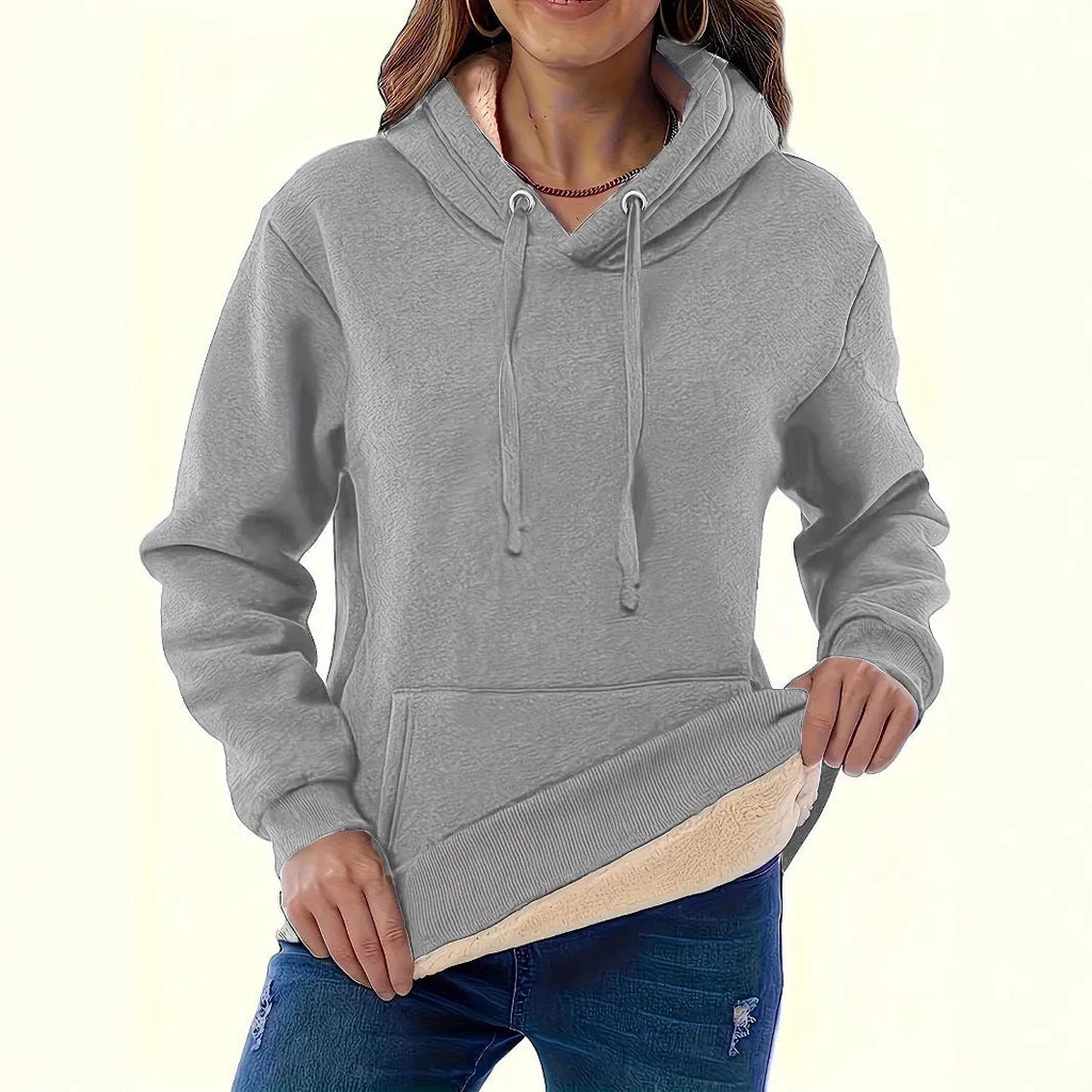Woman wearing a thick, grey hooded sweater with a raised 3D pattern, featuring long sleeves and pockets.