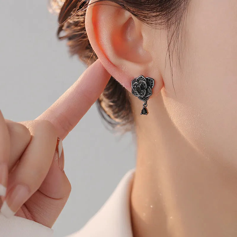 Close-up of women's floral stud earrings with a black rose zircon stone and gold electroplated finish.