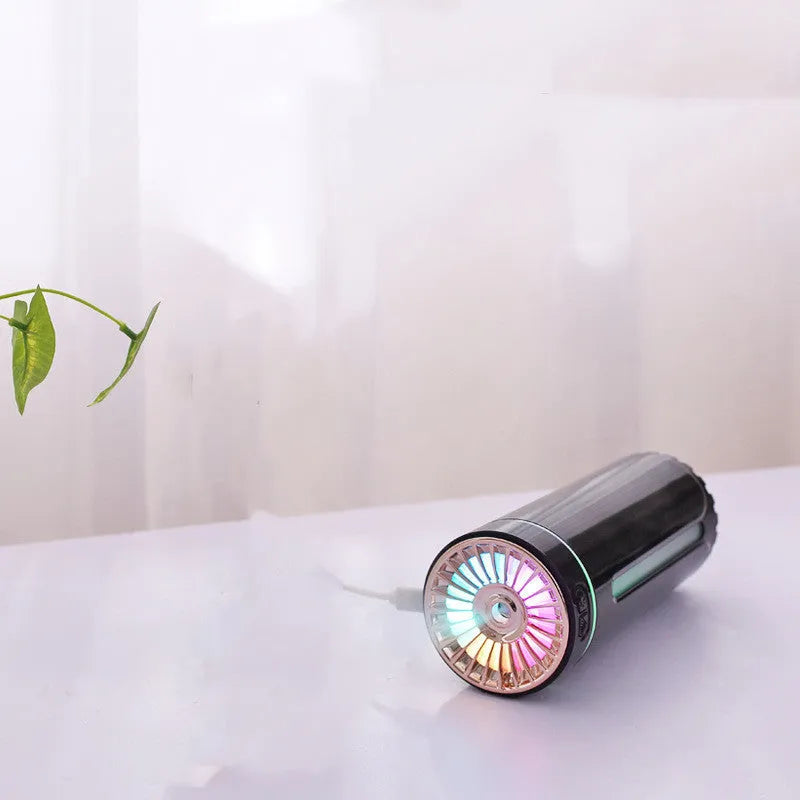 Black portable USB rechargeable car humidifier with colourful lights on a desk next to a cup