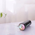 Black portable USB rechargeable car humidifier with colourful lights on a desk next to a cup