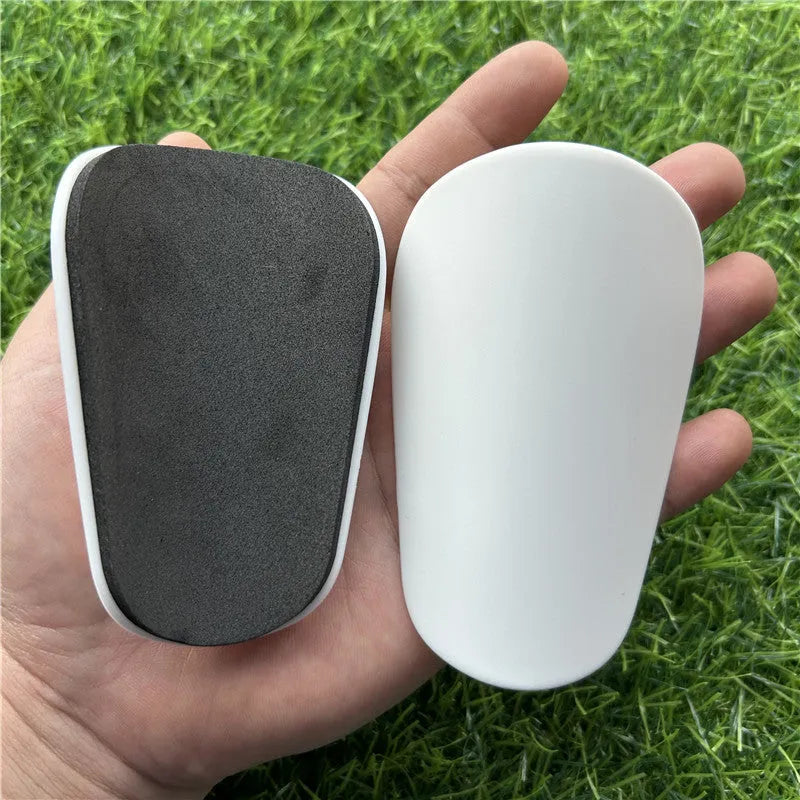 Extra small black and white plastic football shin guards for junior players, size 8cm by 5cm.