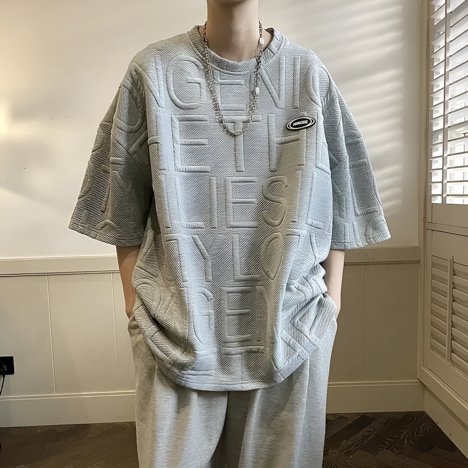 Grey men's loose fit t-shirt with a retro-style three-dimensional raised letter print on the front.