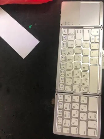 Black tri-fold folding Bluetooth keyboard with touchpad shown open and closed, next to a mobile phone