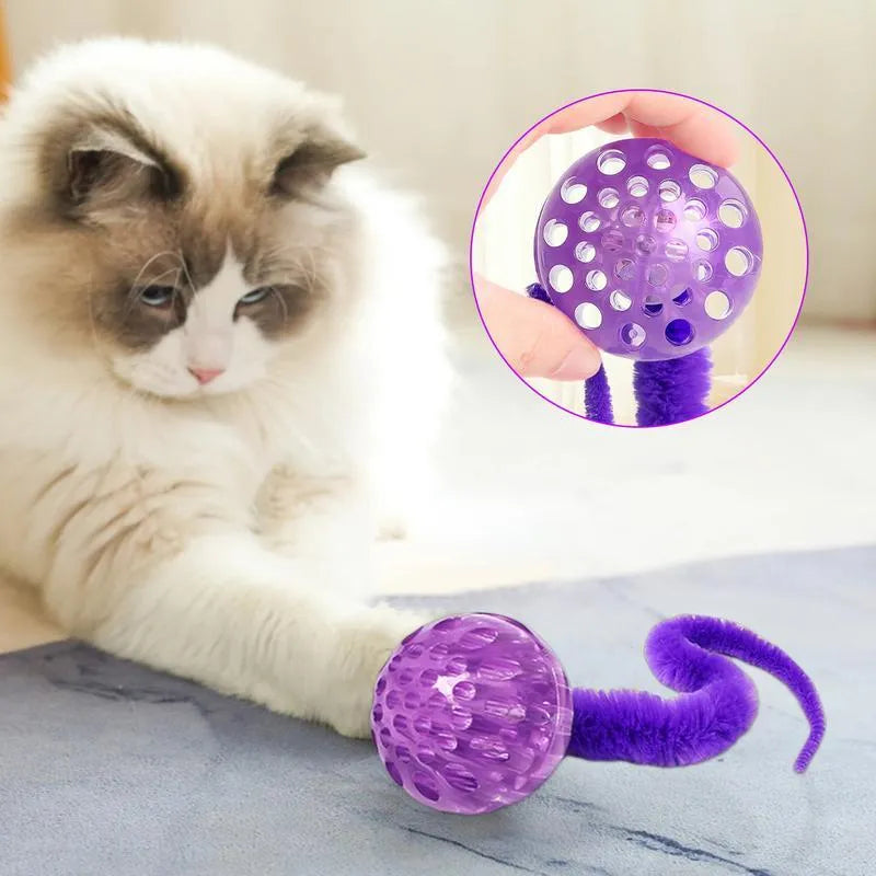 Green TPR bouncy cat toy with a long plush tail on a wooden floor.