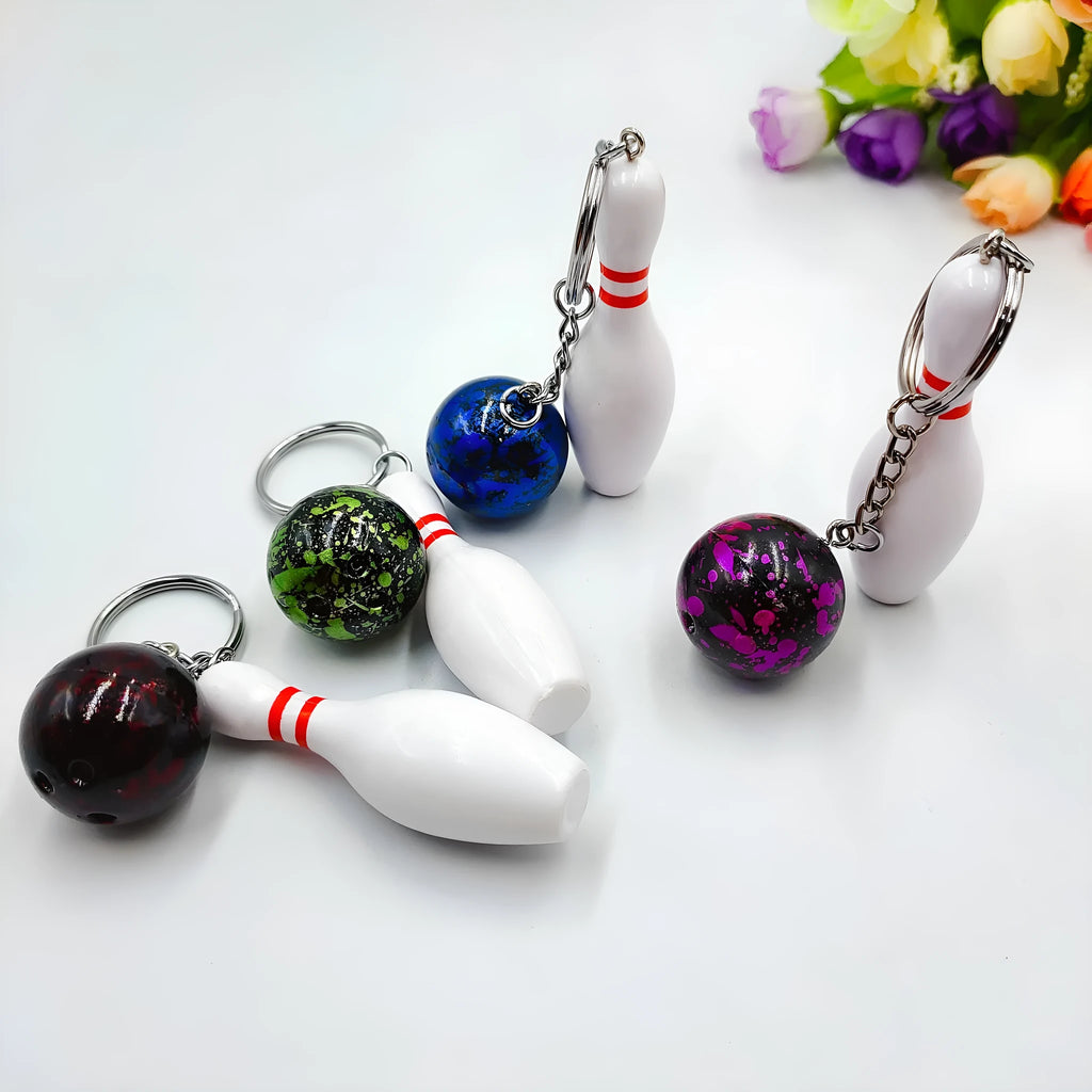 Miniature blue bowling ball keychain pendant with metal keyring on a dark surface.