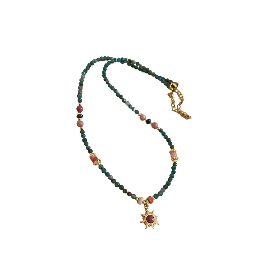 Freshwater pearl necklace with a geometric stone sun pendant on a gold, blue, and pink chain.