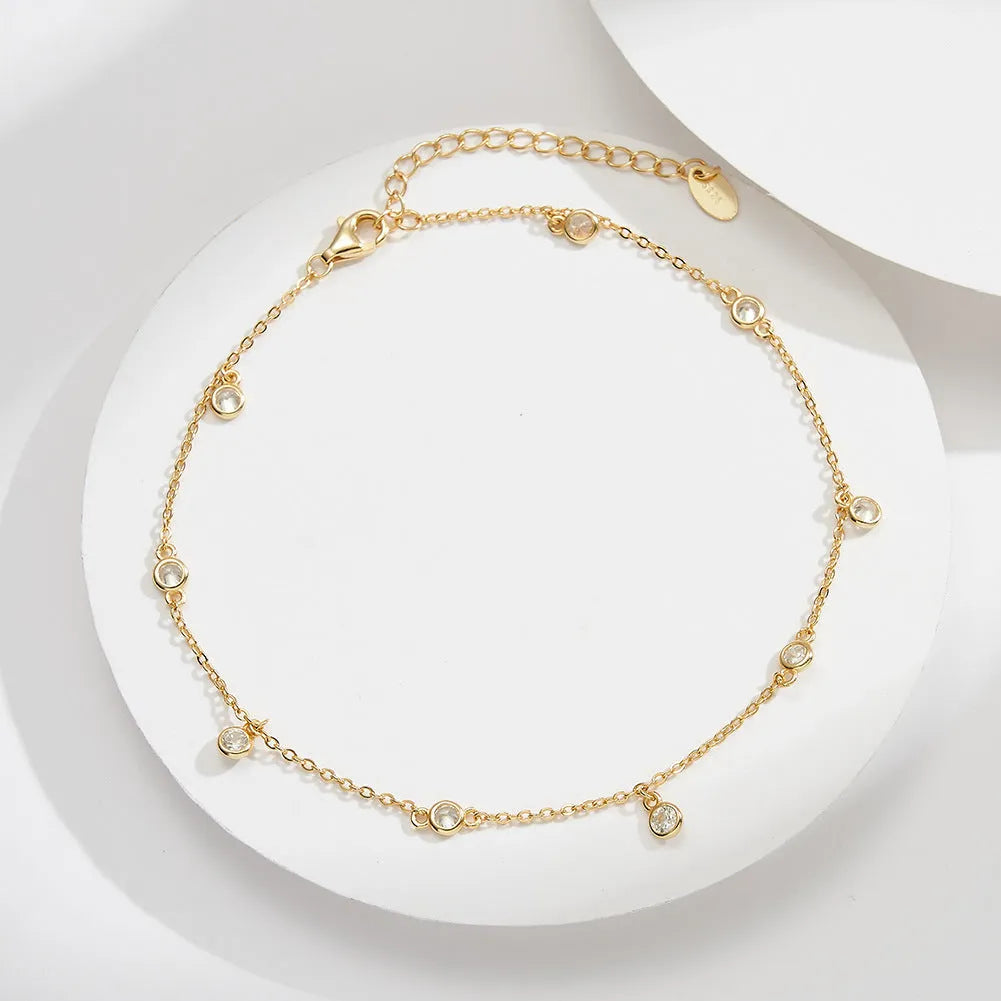Women's sterling silver geometric zirconium pendant anklet on ankle, showing gold and white gold colour options.