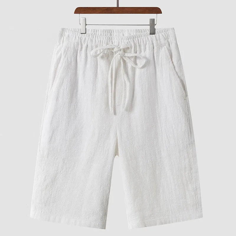 Men's beige linen shorts with loose cropped fit and elasticated waistband laid flat.