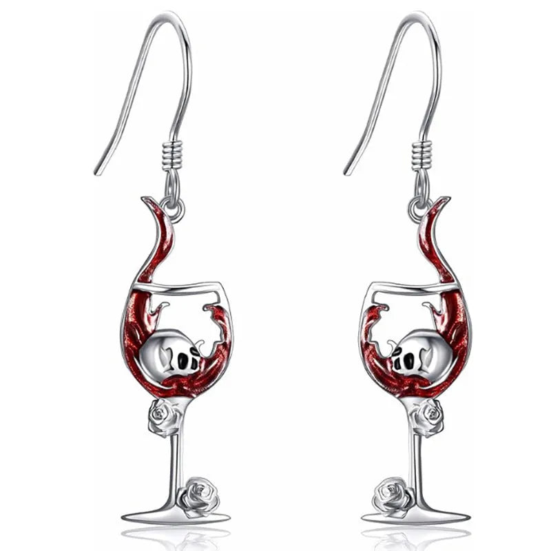 A pair of silver-toned Halloween earrings combining a skull design with a wine glass shape.
