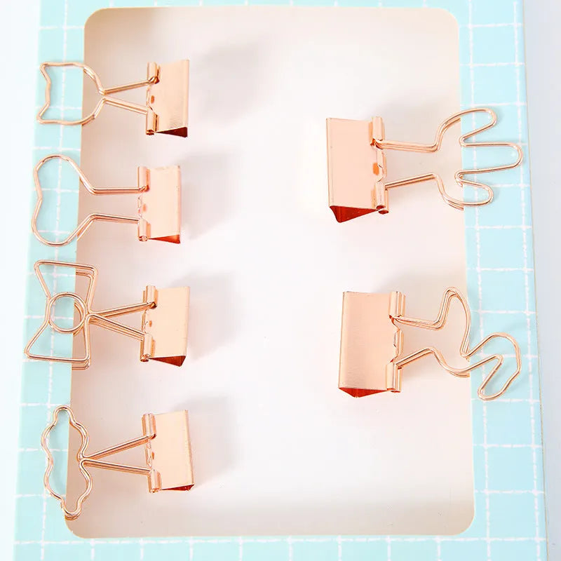 Gold-coloured decorative office paper clips with long tail designs including flamingo, love, cloud, cat, cactus, and bow shapes