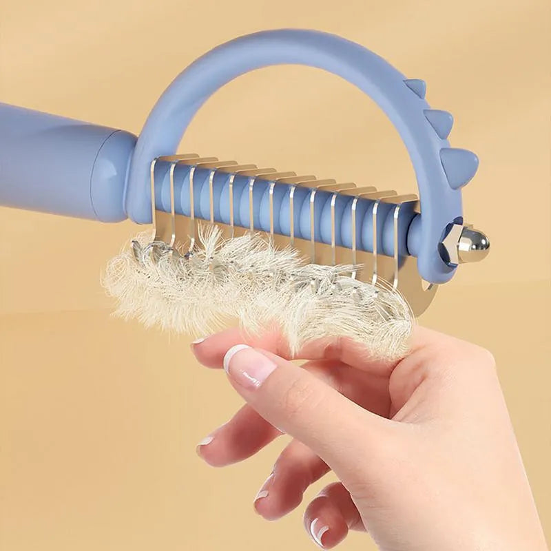 Blue dinosaur-shaped self-cleaning cat brush with stainless steel bristles on a white background.