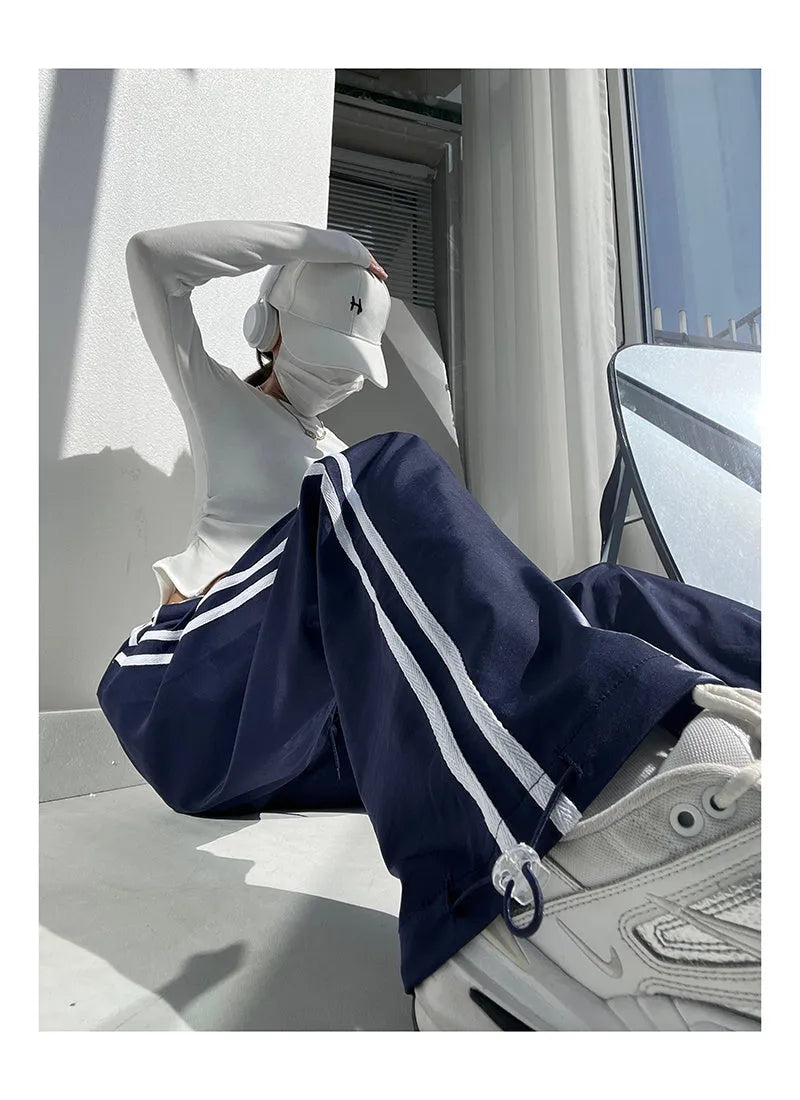 Navy blue loose straight-leg trousers with ribbon-adjustable waist and parallel bars design detail.