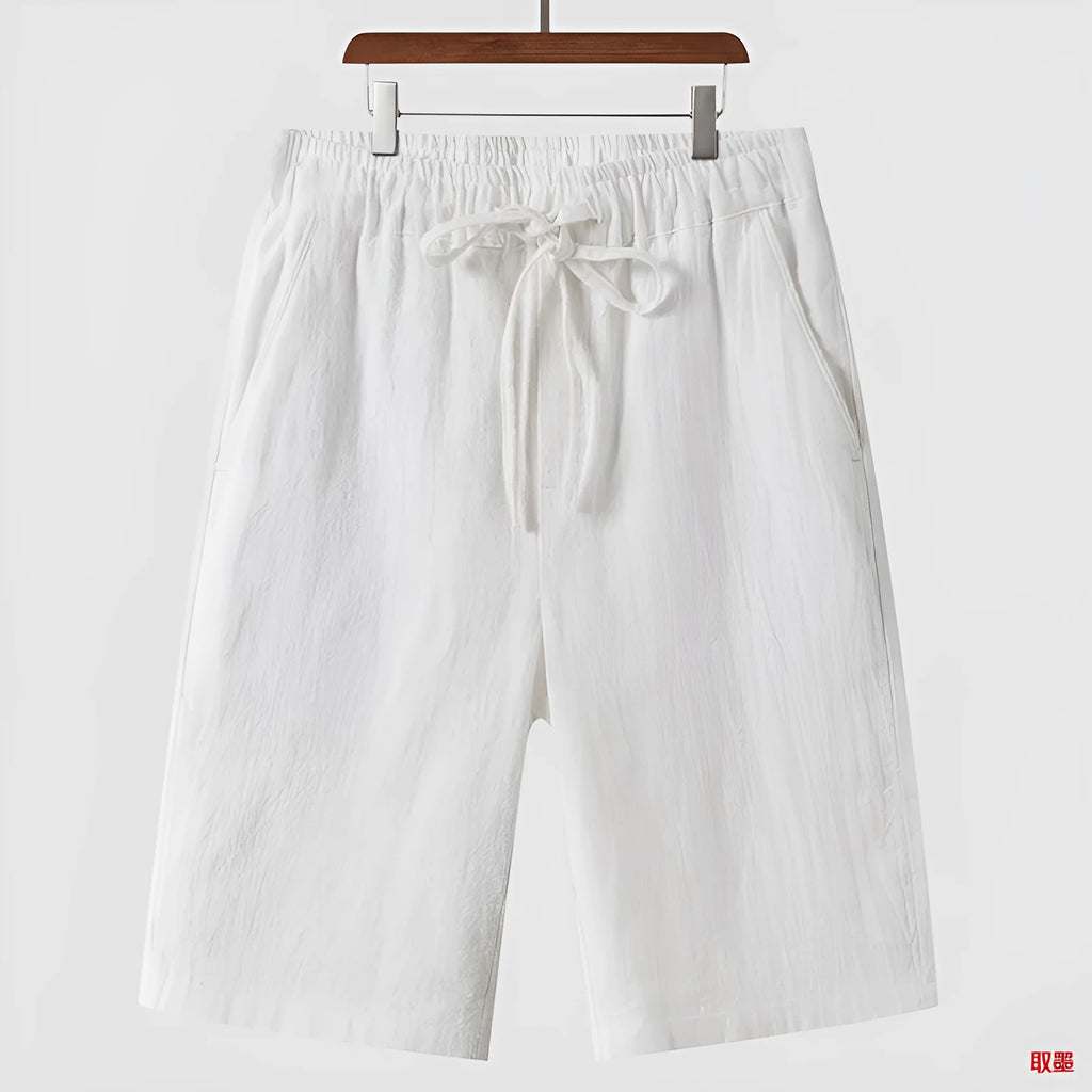 Men's beige linen shorts with loose cropped fit and elasticated waistband laid flat.