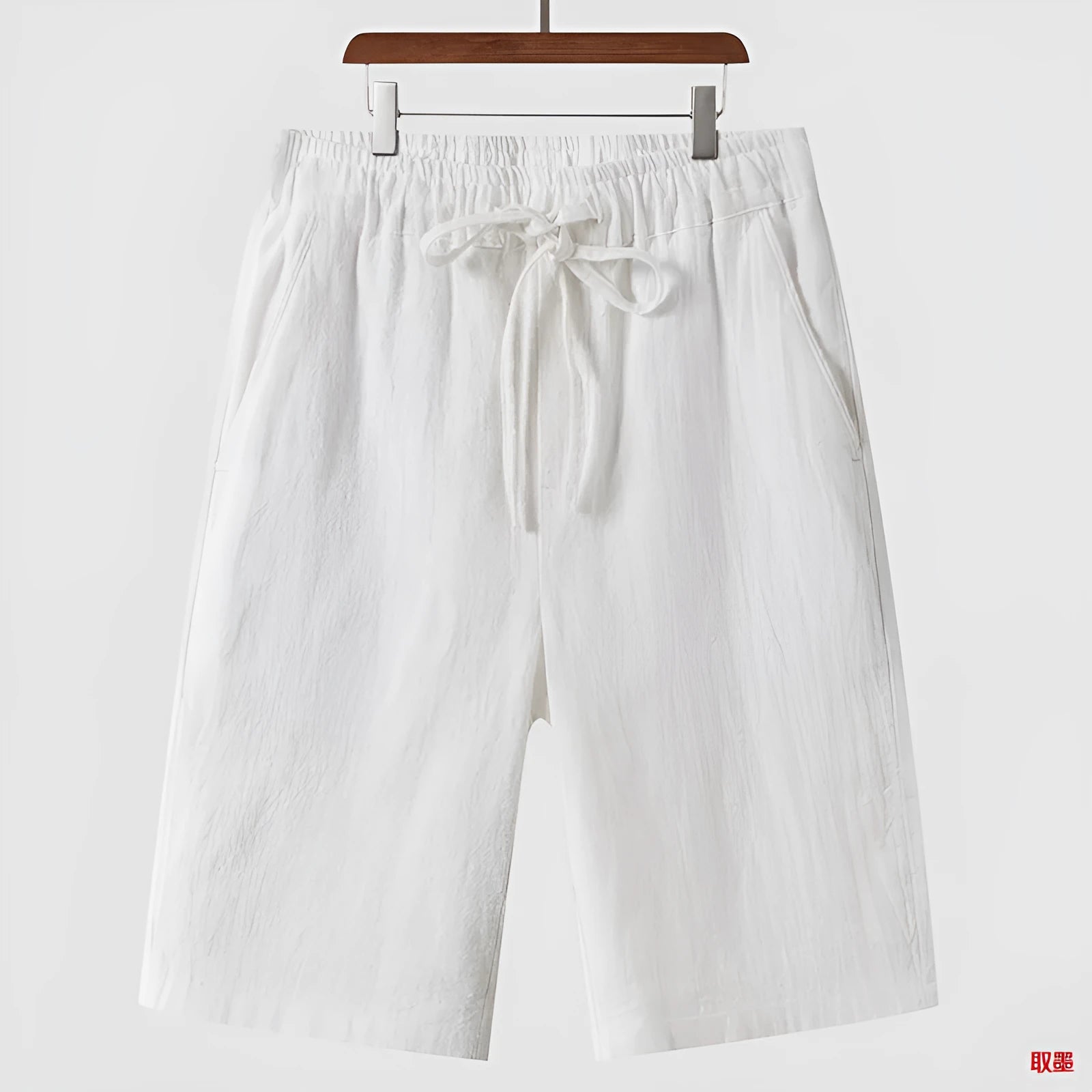 Men's beige linen shorts with loose cropped fit and elasticated waistband laid flat.
