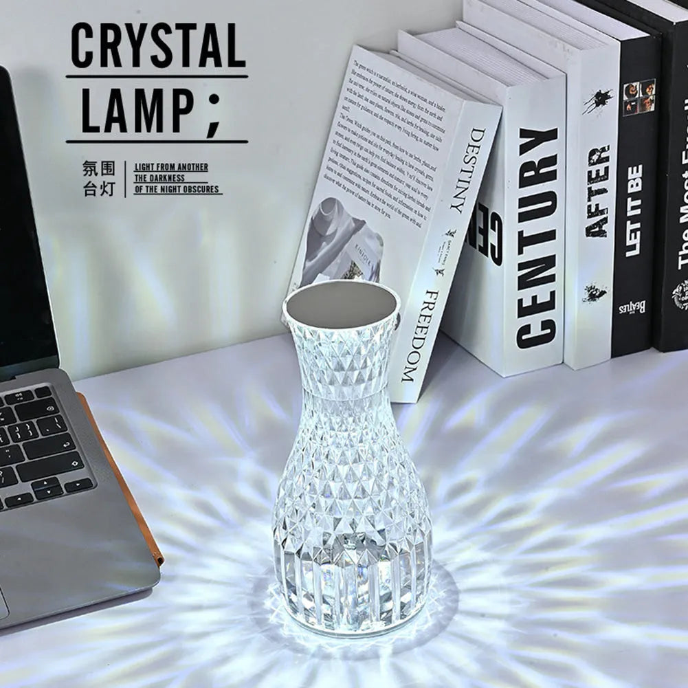 White crystal vase-shaped table lamp with remote control on a wooden surface.