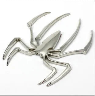 Three-dimensional zinc alloy spider bumper sticker in metallic colours on a surface.