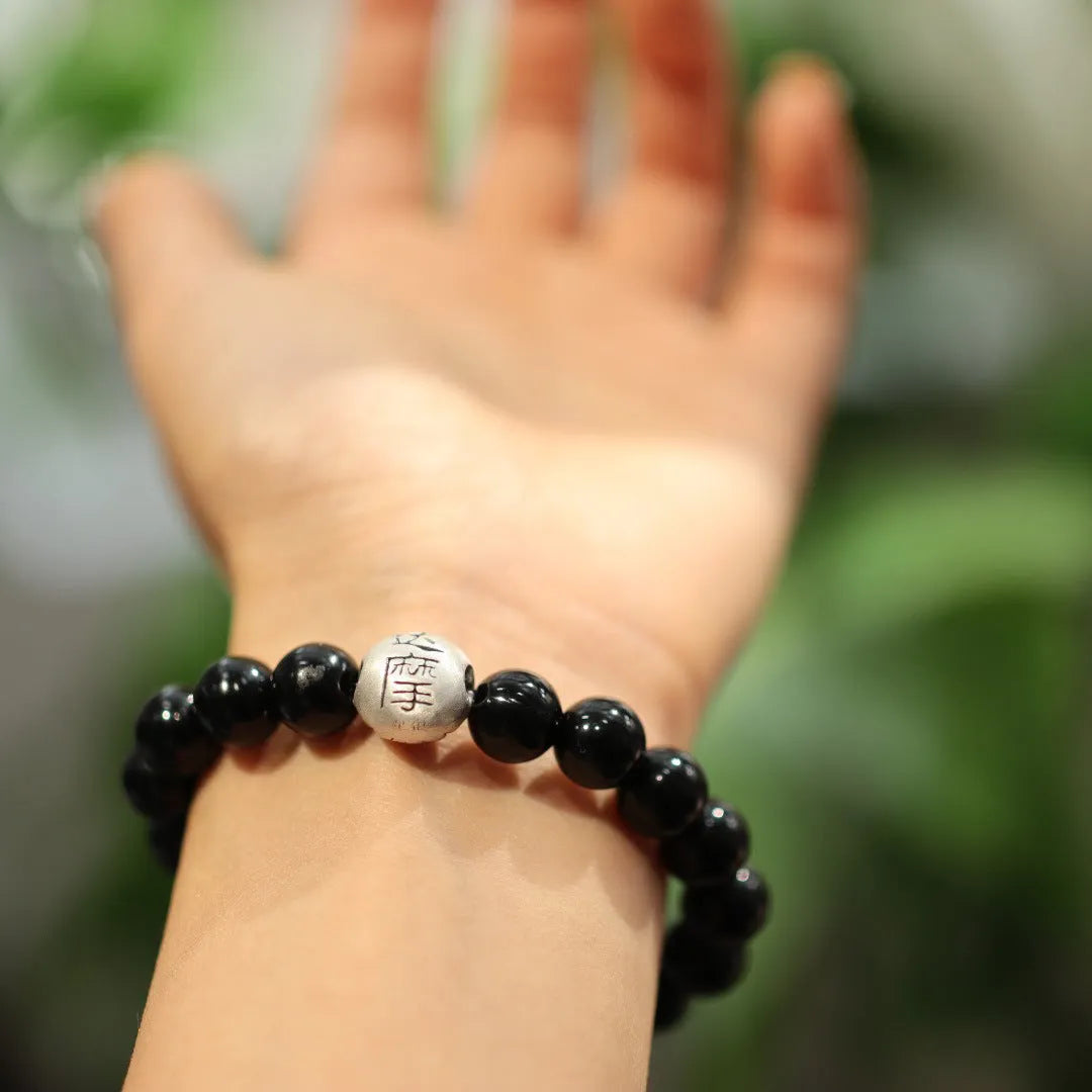 Close-up of a black agate bead bracelet with a sterling silver clasp on a wrist.