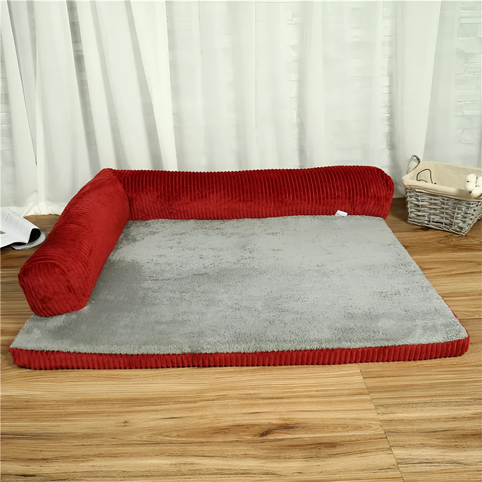 Corduroy dog sofa bed with bolster, shown in grey, placed on a wooden floor.