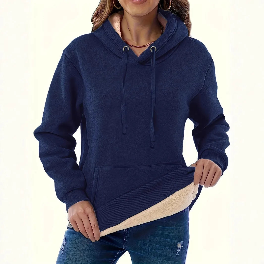 Woman wearing a thick, grey hooded sweater with a raised 3D pattern, featuring long sleeves and pockets.