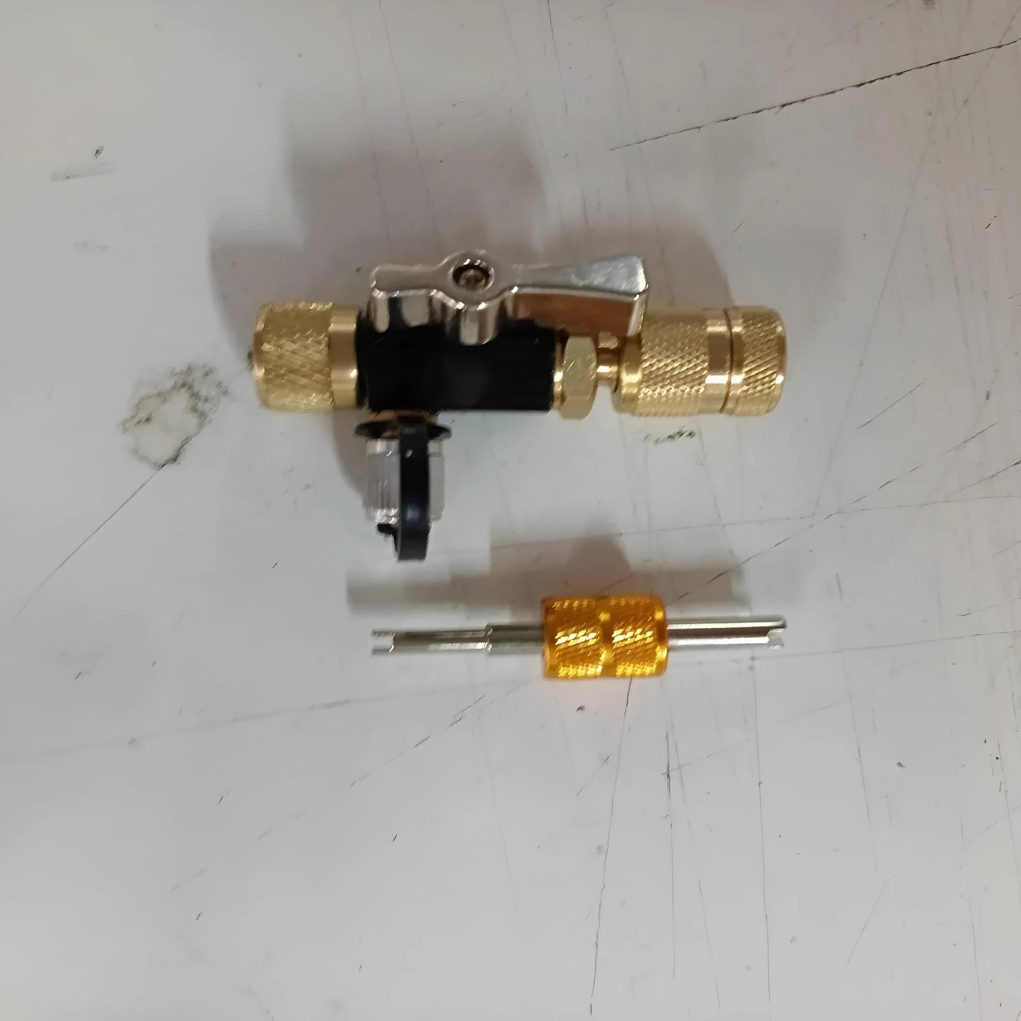 Metal vacuum valve core disassembly tool set showing black and pink valve removers and a valve core wrench on a workshop bench.