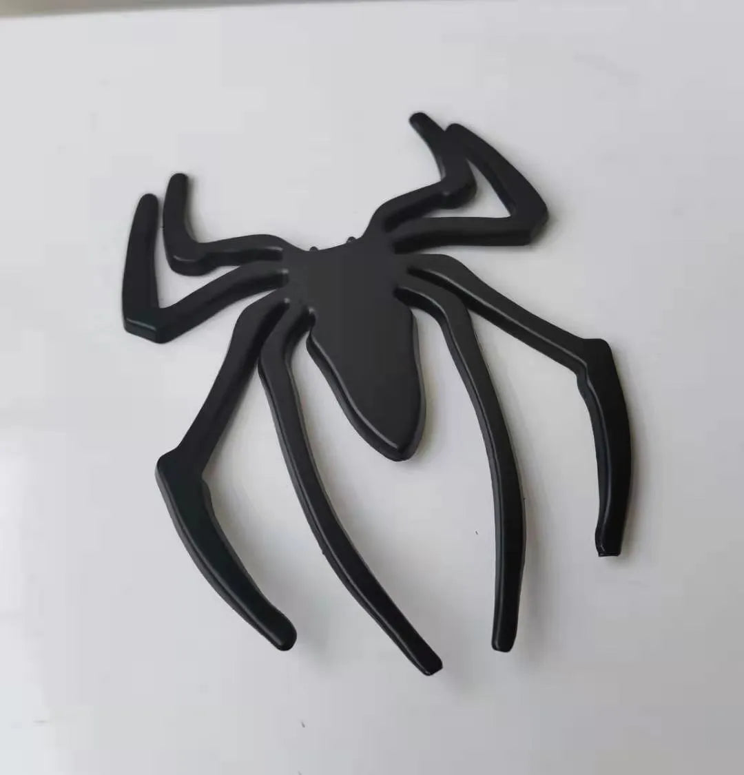 Three-dimensional zinc alloy spider bumper sticker in metallic colours on a surface.